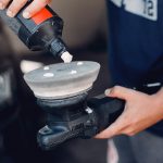 Man in a garage. Worker polish a car.